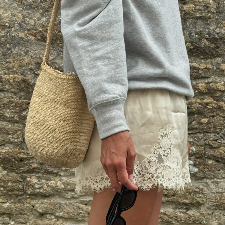 Γυναικείο look με γκρι φούτερ, σαμπανιζέ σατέν σορτς με δαντέλα και ψάθινη τσάντα-πουγκί.