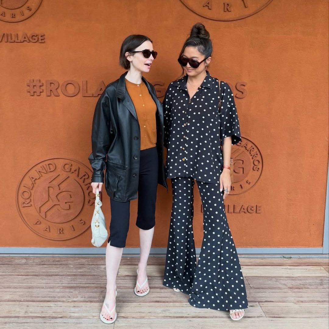 Η Lily Collins στο Roland Garros με τερακότα πλεκτή ζακέτα, μαύρο δερμάτινο τζάκετ Saint Laurent και λευκή δερμάτινη τσάντα ώμου Saint Laurent.