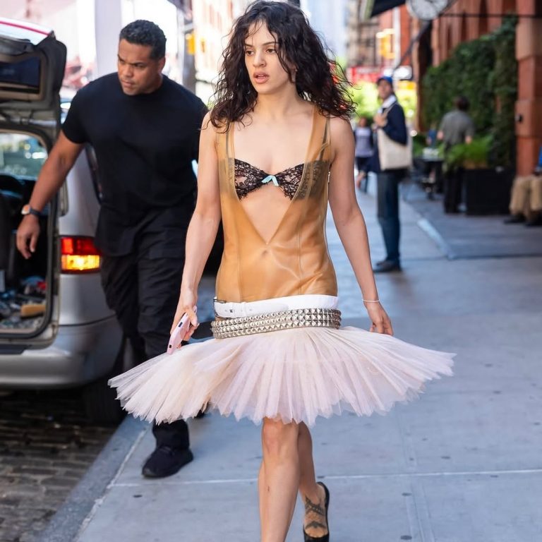 Η Rosalía περπατά στο δρόμο με custom Yasmina look, φορώντας latex bodysuit, τούλινη τουτού με low-rise ζώνες με τρουκς και μαύρες platform pumps.