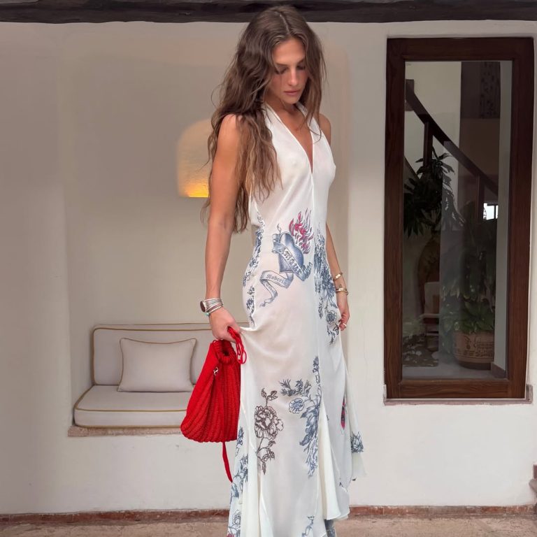 Κοπέλα με λευκό ημιδιάφανο μάξι φόρεμα με κόκκινα και μπλε φλοράλ σχέδια και tattoo prints, μπορντό wedge σαγιονάρες και έντονη κόκκινη τσάντα-πουγκί.