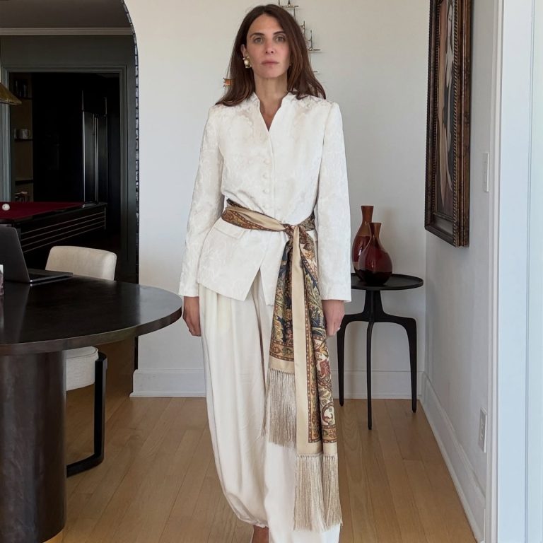 Ένα καλοκαιρινό look σε ουδέτερους τόνους, όπου μια κοπέλα φοράει ένα φαρδύ παντελόνι και έχει δέσει γύρω από τη μέση της ένα αέρινο μαντήλι με μακριά κρόσσια, δίνοντας κίνηση και ένα ανεπιτήδευτο boho-chic twist στο outfit.