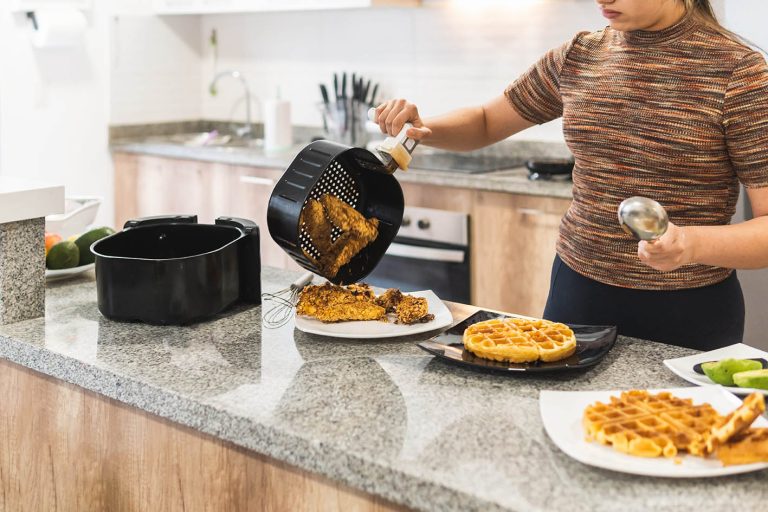 Μήπως χρησιμοποιείτε λάθος το air fryer σας; Τα μυστικά για αληθινά τραγανό φαγητό χωρίς λάδι Στη φωτογραφία γυναίκα που σερβίρει τηγανητό κοτόπουλο με βάφλες από τη φριτέζα αέρα