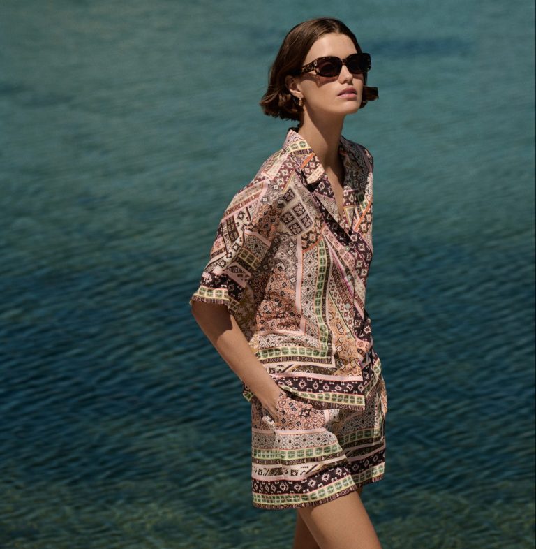 Γυναίκα μοντέλο φοράει printed co-ord σετ Marks & Spencer με καλοκαιρινά μοτίβα, ποζάροντας με φόντο τη θάλασσα.