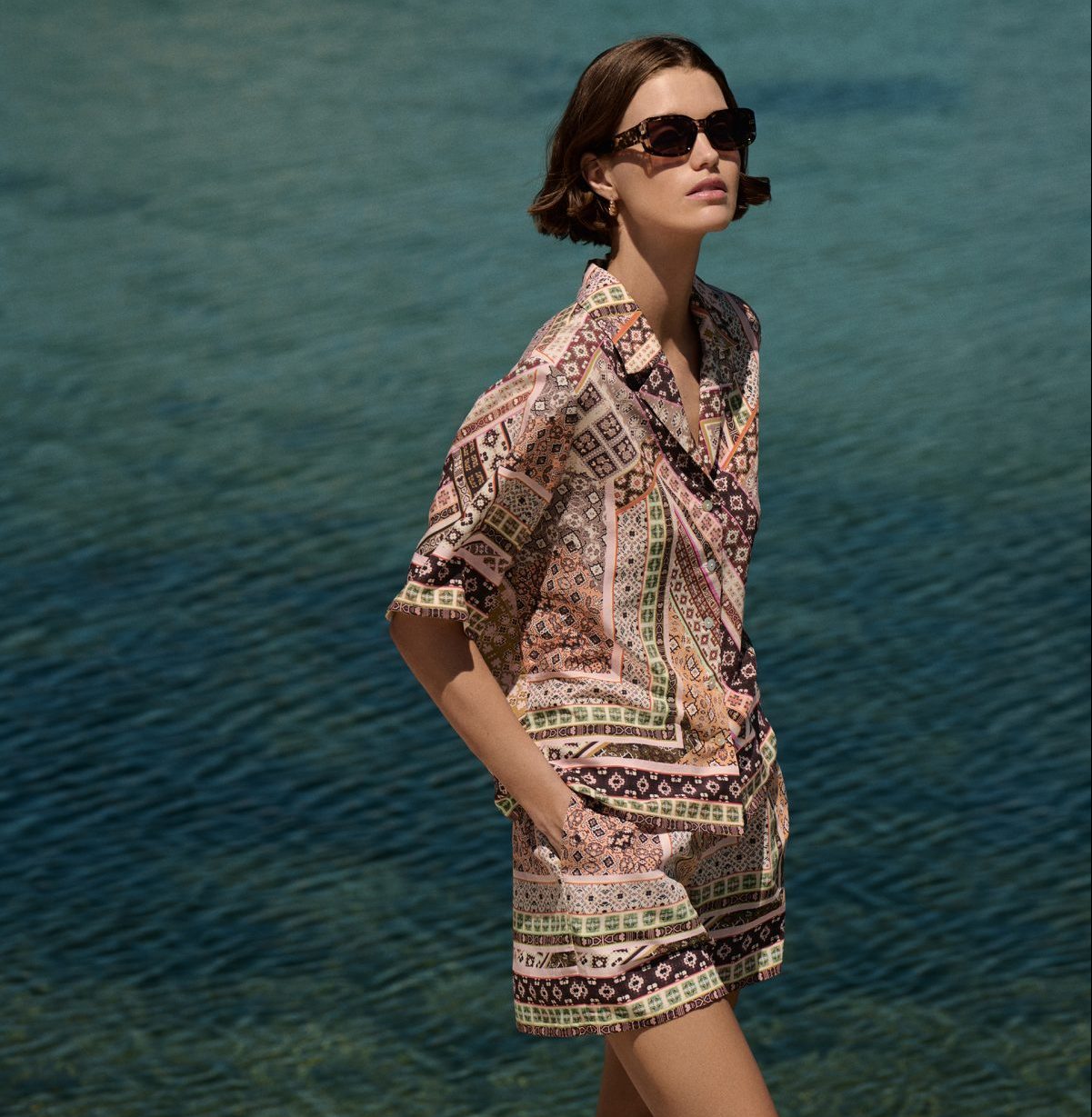 Γυναίκα μοντέλο φοράει printed co-ord σετ Marks & Spencer με καλοκαιρινά μοτίβα, ποζάροντας με φόντο τη θάλασσα.