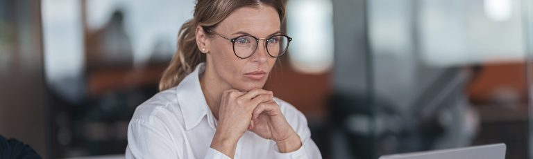 Σοβαρή επιχειρηματίας με γυαλιά που εργάζεται στο φορητό υπολογιστή στο χώρο εργασίας στο σύγχρονο γραφείο