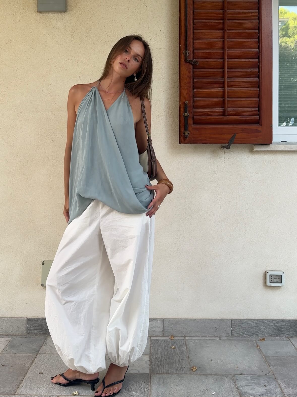 Αέρινο καλοκαιρινό look με ντραπέ τοπ, voluminous λευκό παντελόνι και κομψά μαύρα kitten heels.
