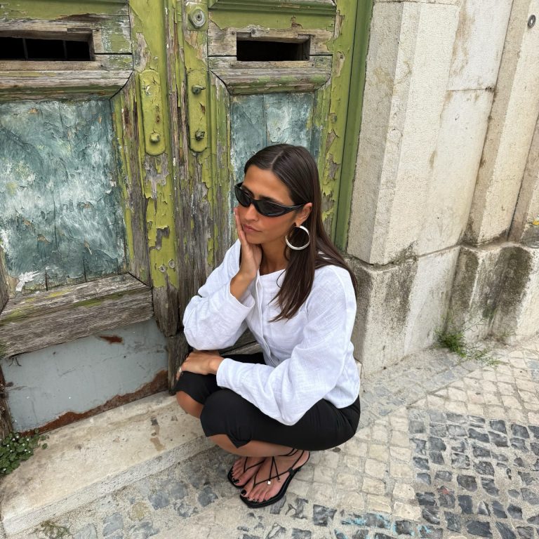 Γυναίκα με μαύρο κάπρι παντελόνι και μαύρα μινιμαλιστικά πέδιλα με λουράκια, σε συνδυασμό με λευκό λινό πουκάμισο.