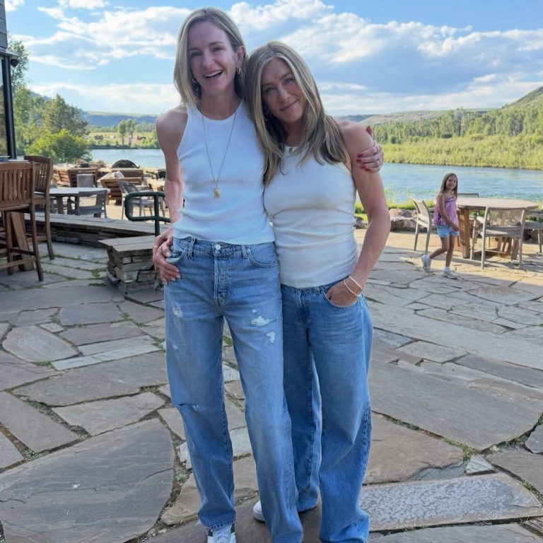 Η Jennifer Aniston με λευκό ριμπ tank τοπ και φαρδύ τζιν παντελόνι αγκαλιάζει μια φίλη της με παρόμοιο look σε εξωτερικό χώρο.