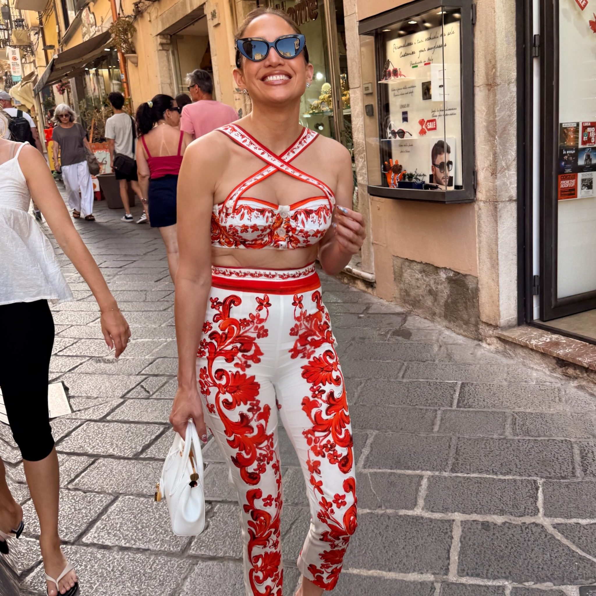 H Jennifer Lopez με λευκό και κόκκινο εμπριμέ σύνολο, λευκή τσάντα και γυαλιά ηλίου.