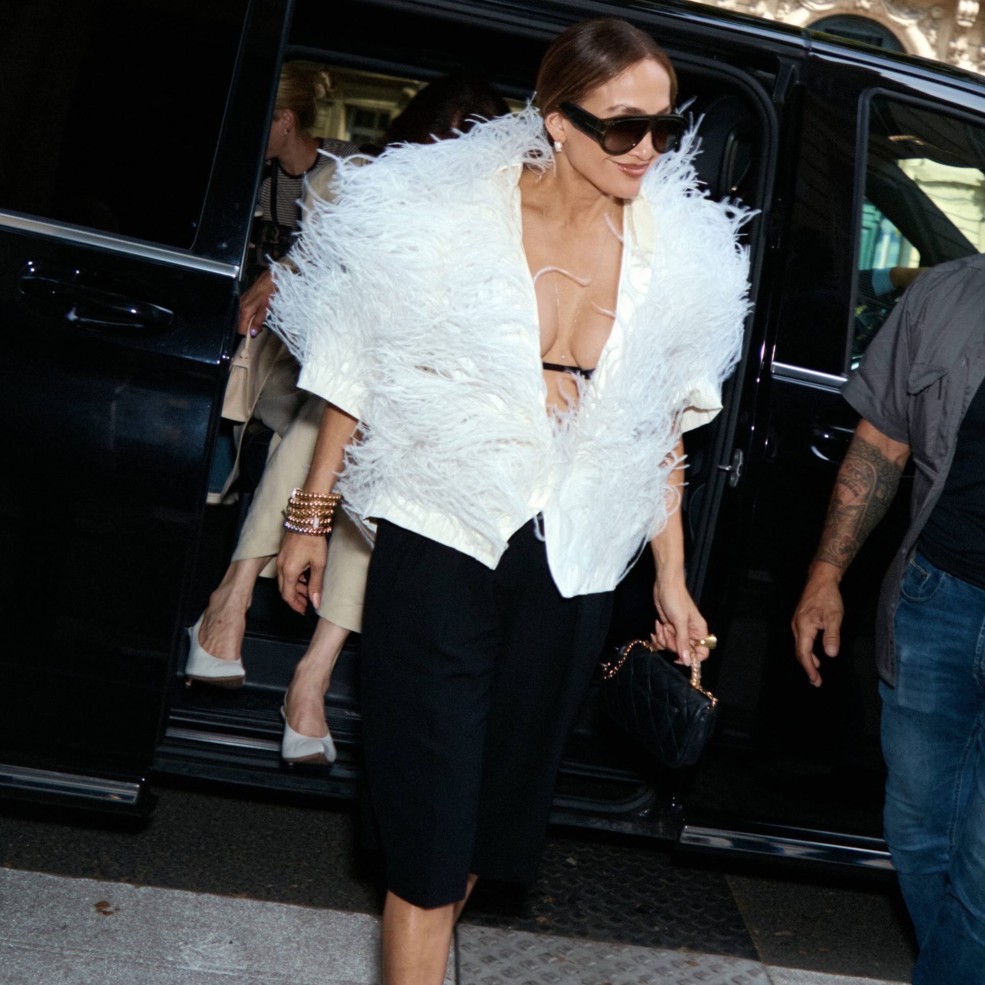 Η Jennifer Lopez με λευκό feathered τοπ, μαύρη βερμούδα και γυαλιά ηλίου.