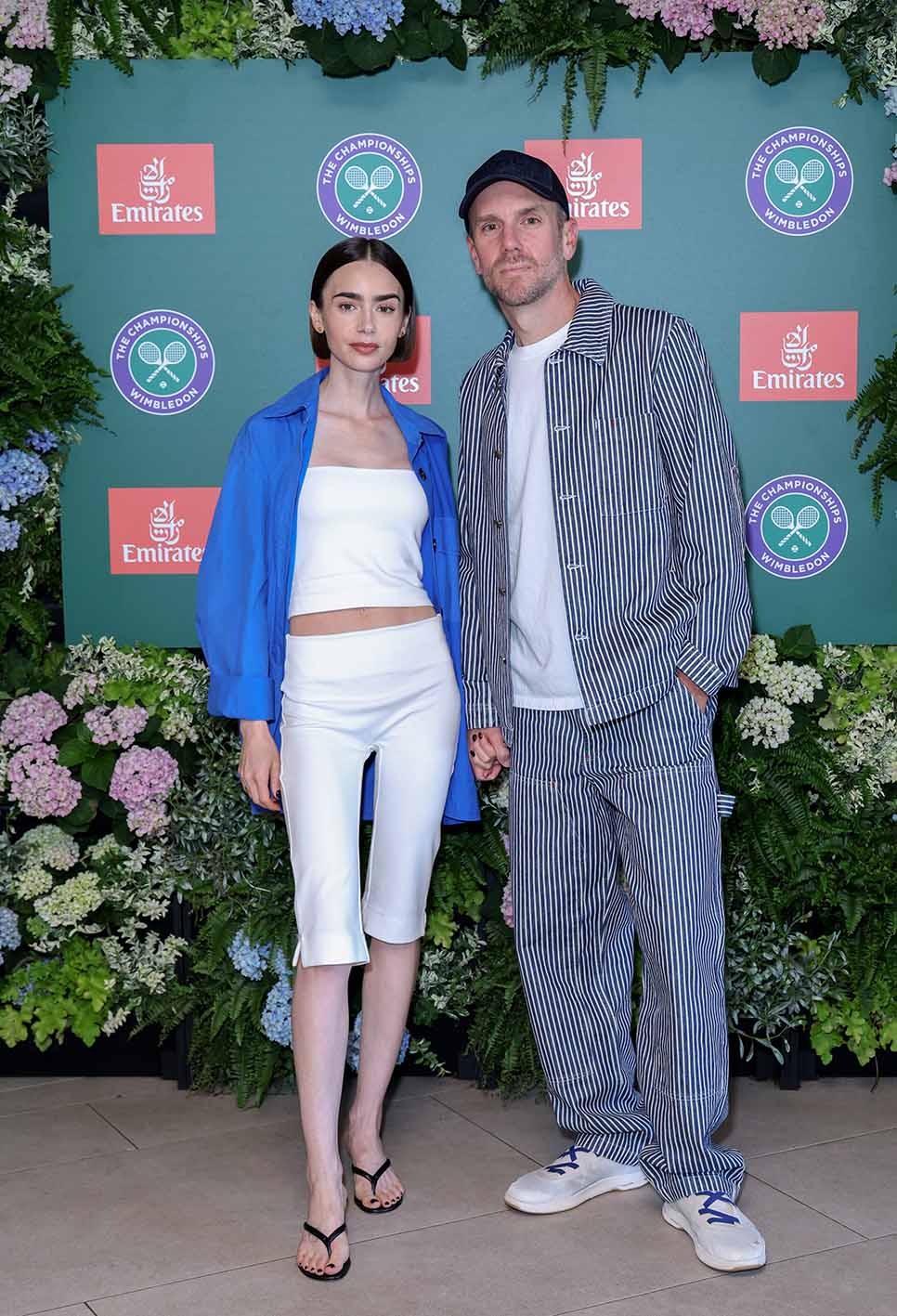H Lily Collins με λευκό σύνολο και μπλε πουκάμισο στο Wimbledon. Μαζί της και ο Charlie McDowell στο All England Lawn Tennis and Croquet Club στις 12 Ιουλίου 2026 στο Λονδίνο.