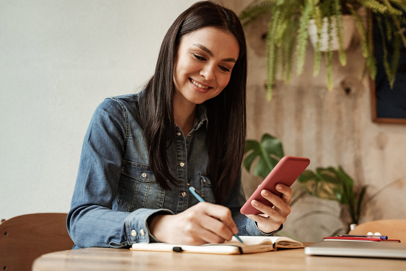 Χαρούμενη γυναίκα που κρατά smartphone και γράφει σε σημειωματάριο