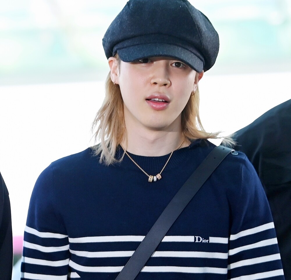 Ο Jimin με Dior σε ένα effortless airport look, συνδυάζοντας ριγέ μπλε και λευκό μάλλινο sweater με μπλε denim jeans. Ολοκλήρωσε την εμφάνισή του με μαύρη δερμάτινη Dior Archie zipped bag και ένα εντυπωσιακό My Dior κολιέ από κίτρινο, ροζ και λευκό χρυσό, διακοσμημένο με διαμάντια.