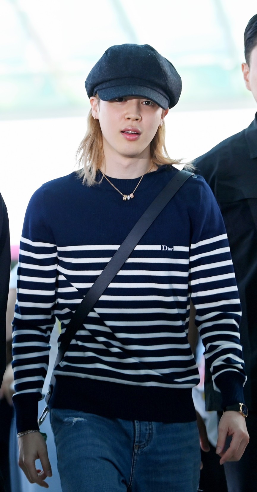 Ο Jimin με Dior σε ένα effortless airport look, συνδυάζοντας ριγέ μπλε και λευκό μάλλινο sweater με μπλε denim jeans. Ολοκλήρωσε την εμφάνισή του με μαύρη δερμάτινη Dior Archie zipped bag και ένα εντυπωσιακό My Dior κολιέ από κίτρινο, ροζ και λευκό χρυσό, διακοσμημένο με διαμάντια.