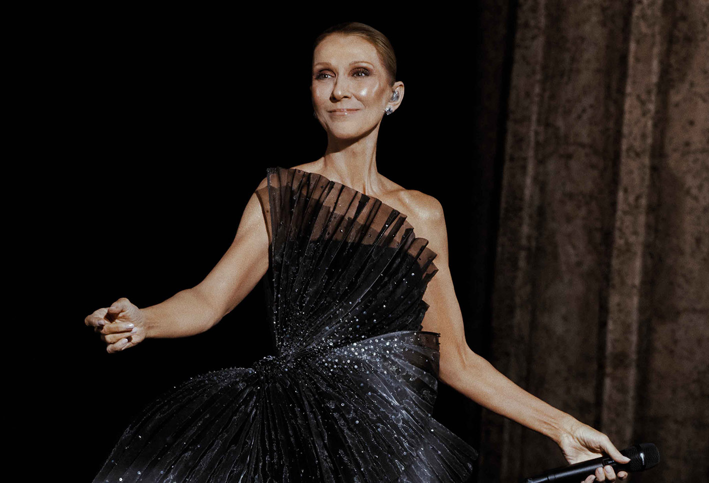 Η Céline Dion φόρεσε ένα μακρύ Dior φόρεμα από μουσελίνα, σε ασύμμετρη γλυπτική σιλουέτα, με πλισέ σε μαύρο και ανοιχτό γκρι, κεντημένο με κρύσταλλα και πέρλες, καθώς και μια ιδιαίτερη πλισέ κατασκευή στο πλάι της μέσης.