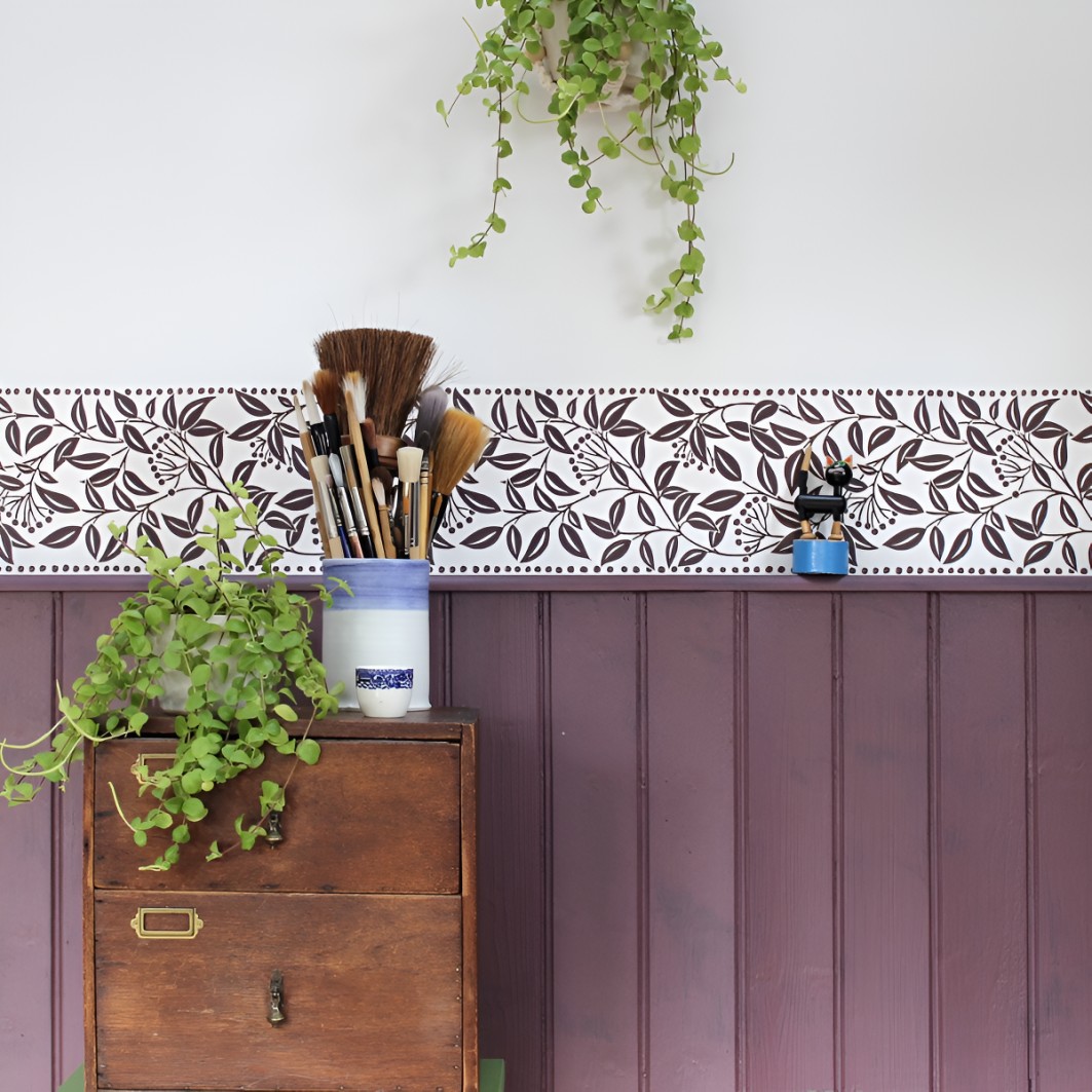 Η ταπετσαρία Jasmine Leaf Border / Bark της Fiona Howard Wallpapers συνδυάζει ένα λεπτό, στριφογυριστό κλαδί με φύλλα σε καφέ απόχρωση πάνω σε λευκό φόντο.