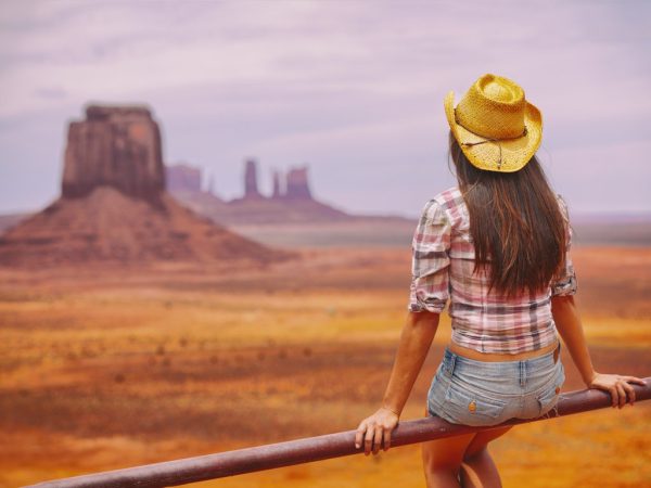Western USA-Cowgirl woman enjoying view of Monument Valley in cowboy hat. Beautiful young girl in outdoors, Arizona Utah, USA. Banner panorama.