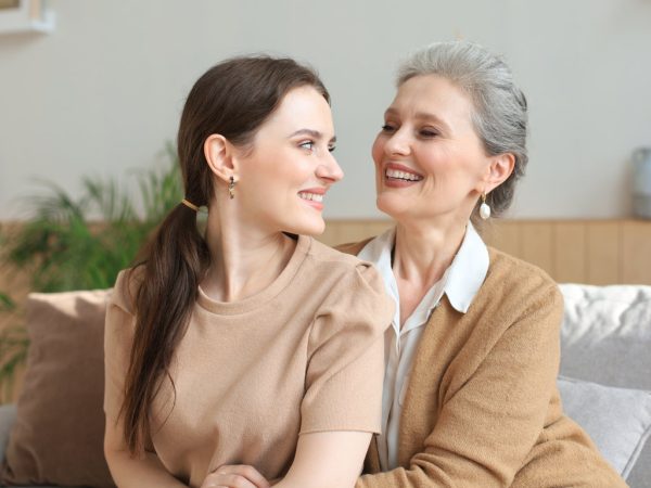 Beautiful mother and daughter. Cheerful young woman is embracing her middle aged mother in living room. Family portrait.