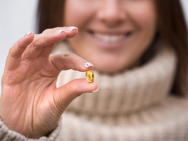 Vitamin D-Smiling woman holding fish oil pill or vitamin D supplement. Taking capsule with omega 3 or D3. Vitamin and dietary supplements. Healthy diet nutrition