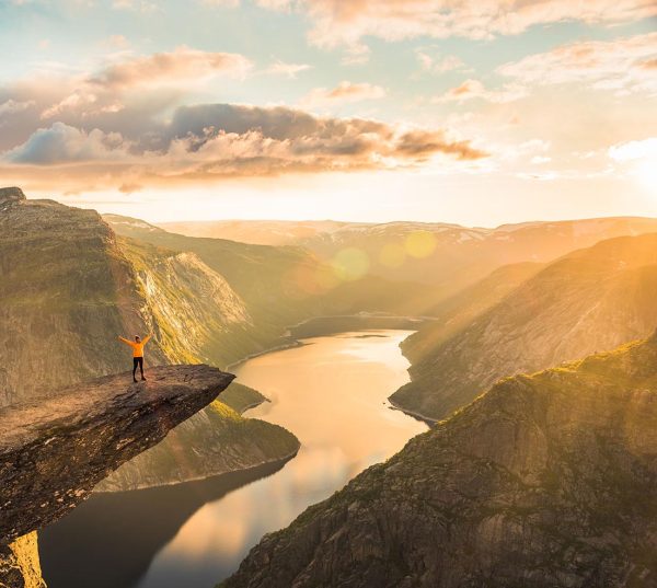 02/09-17, Trolltunga, Norway. A woman is standing on the edge of trolltunga with her side against the sun. The drop down is 700 m.
