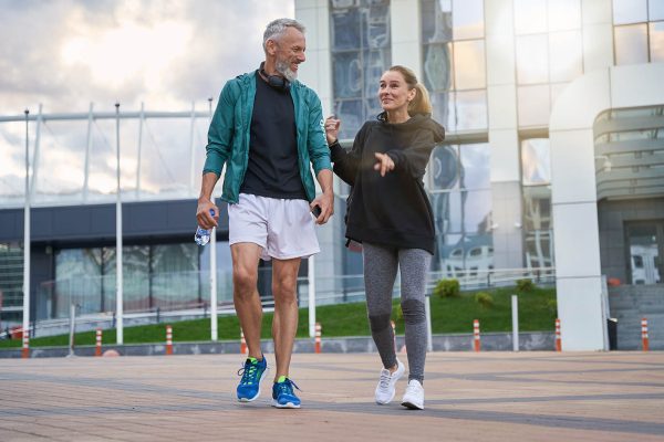 Full length shot of active middle aged couple in sportswear looking cheerful while walking together outdoors after gym workout