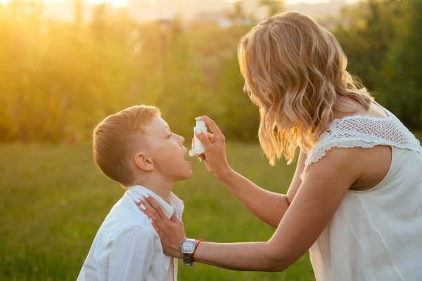 caring mother uses an inhaler to her son in the park