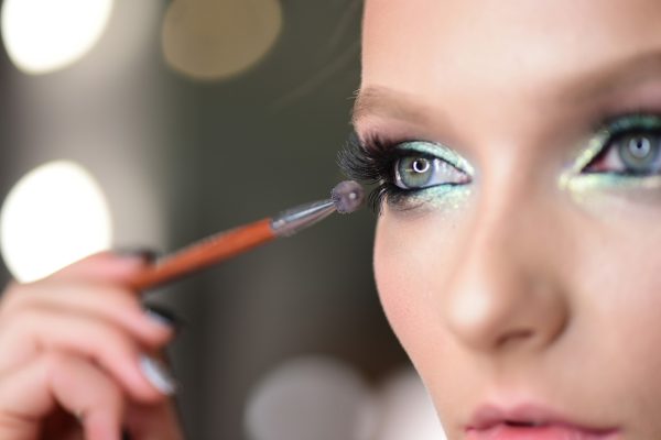 Woman applying black mascara on eyelashes with makeup brush. Young beautiful woman applying mascara makeup on eyes by brush. Beauty girl applying makeup over grey background