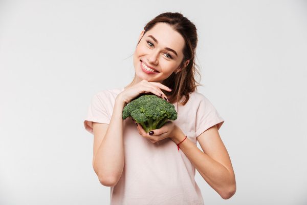 Portrait of a smiling pretty girl holding broccoli