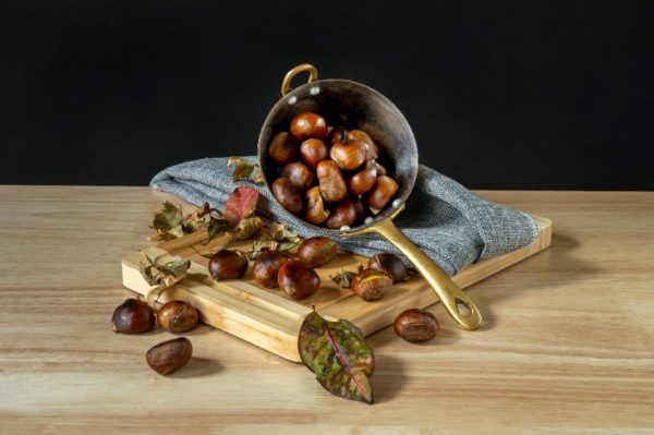 Still life with roasted chestnut casserole on bamboo table and gray cloth