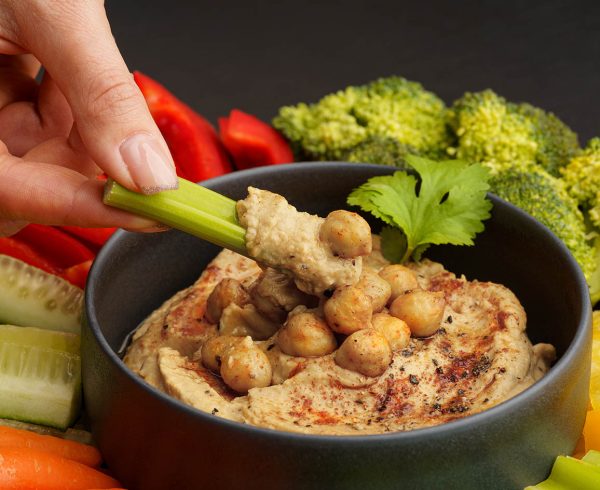 Woman hand taking chickpeas hummus with celery stick. Tasty hummus with fresh vegetables