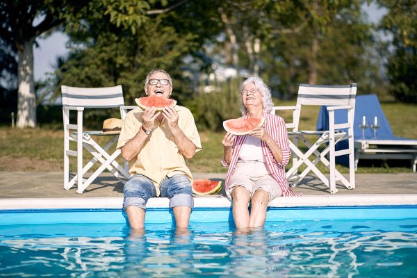 Elderly couple  eating watermelon by the pool.Man and woman enjo