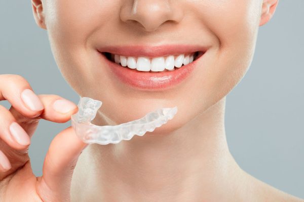 The woman holds in her hand removable invisible transparent aligners, and smiles.