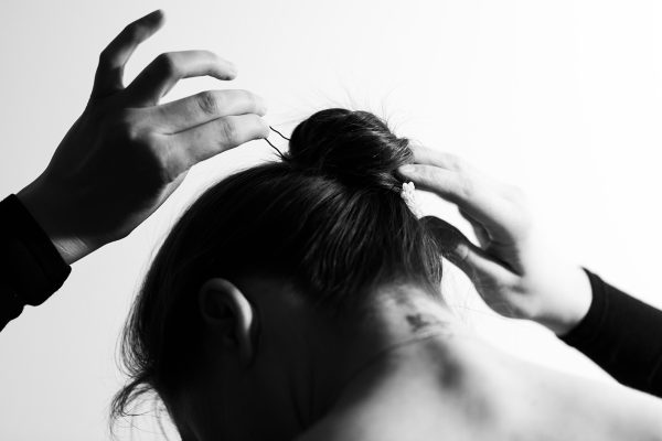 A woman stabs her hair and collects it in a bun. Black and white photo.
