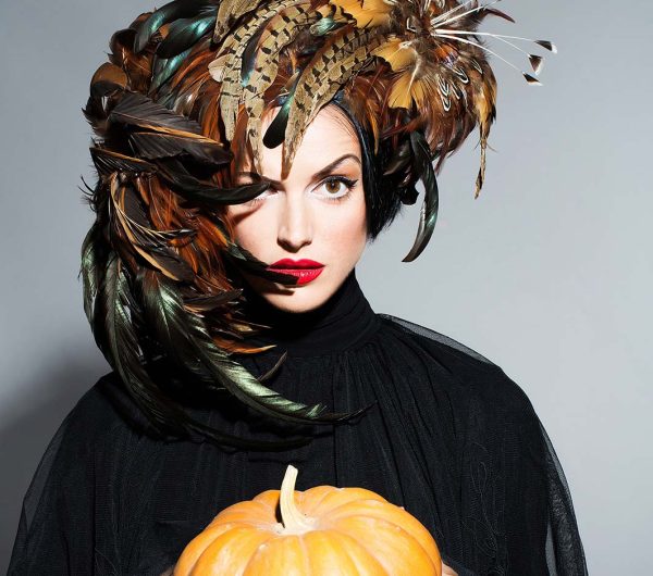 pretty woman in feather hat holds halloween pumpkin