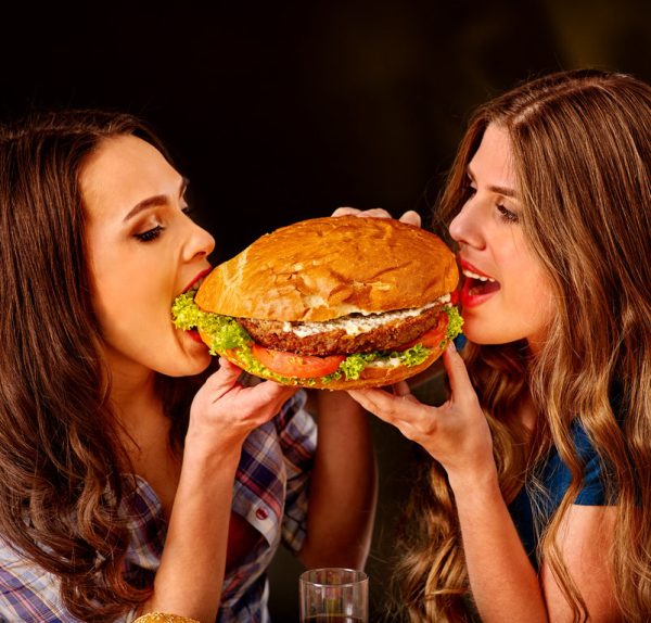 Girl holding and bite big hamburger from different sides. Fastfood concept. Cheeseburger on foreground.