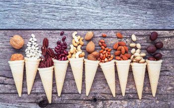 Concept for homemade various nuts ice cream. Mixed nuts in waffle cones on shabby wooden background.top view