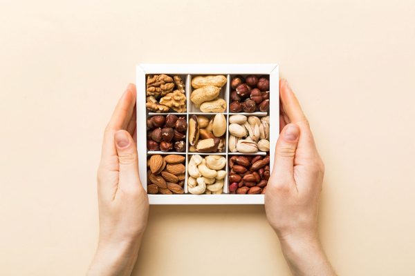 Young woman holding box with different nuts, closeup. Close up, copy space, top view, flat lay. Walnut, pistachios, almonds, hazelnuts and cashews