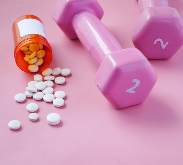 pink color dumbbell and medical pills on pink