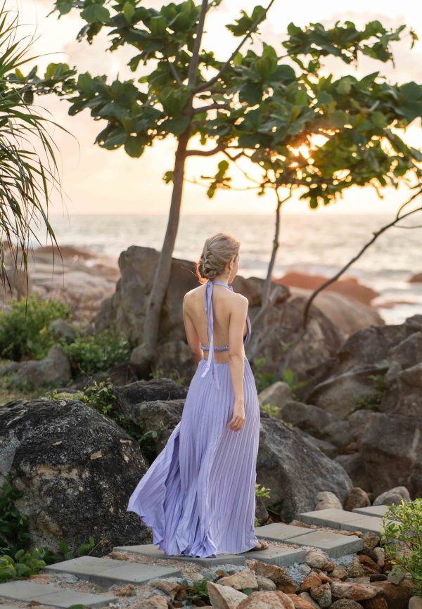 Woman in purple dress walk on a stone walkway at the beach, enjo