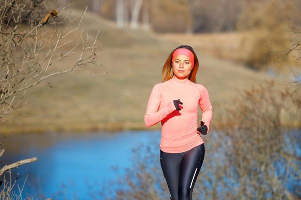 Young woman jogging in the park near the pond in the cold sunny morning