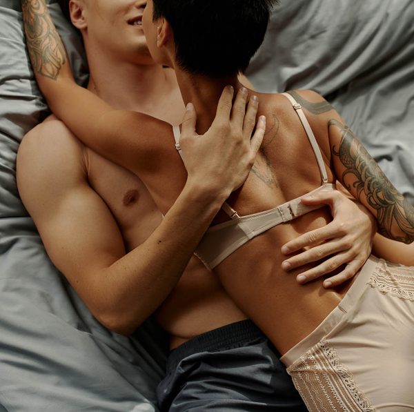 Cropped view of smiling man touching sensual tattooed girlfriend