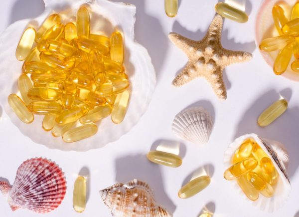 Omega 3 capsules and seashells with long shadows. Top view photo of supplement food with oil of nordic fish. Vitamins and tablets against white.