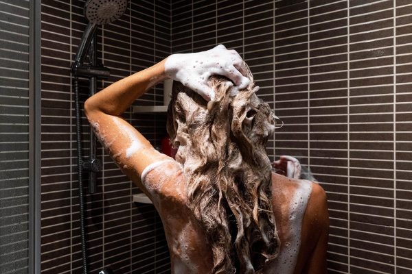 Rear view of naked blonde woman soaping her hair a shower in a bathroom