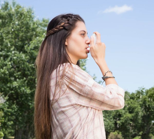 Pretty brunette using her inhaler  on a sunny day