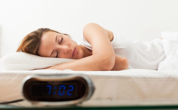 Beautiful sleeping young woman in bad with alarm clock
