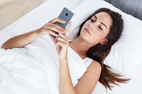 Γυναίκα ξαπλωμένη στο κρεβάτι με το κινητό
