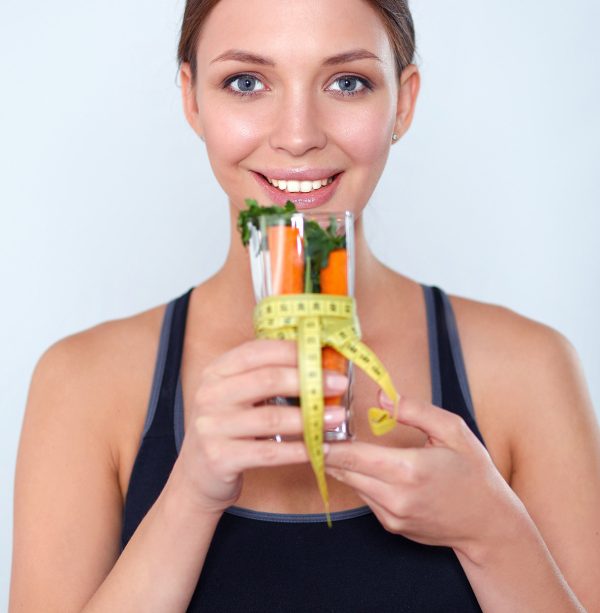 Woman holding a drinking glass full of fresh fruit salad with a tape measure around the glass