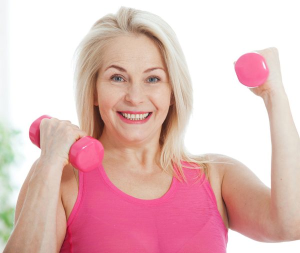 Happy middle aged woman lifting dumbbells at home in the living room
