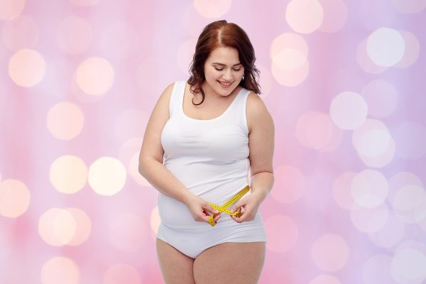 happy young plus size woman with measuring tape