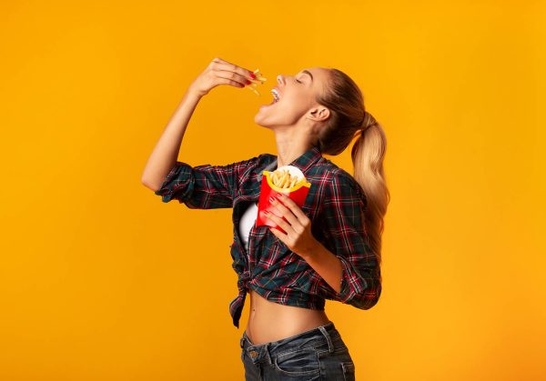 Young Woman Eating French-Fries On Yellow Background